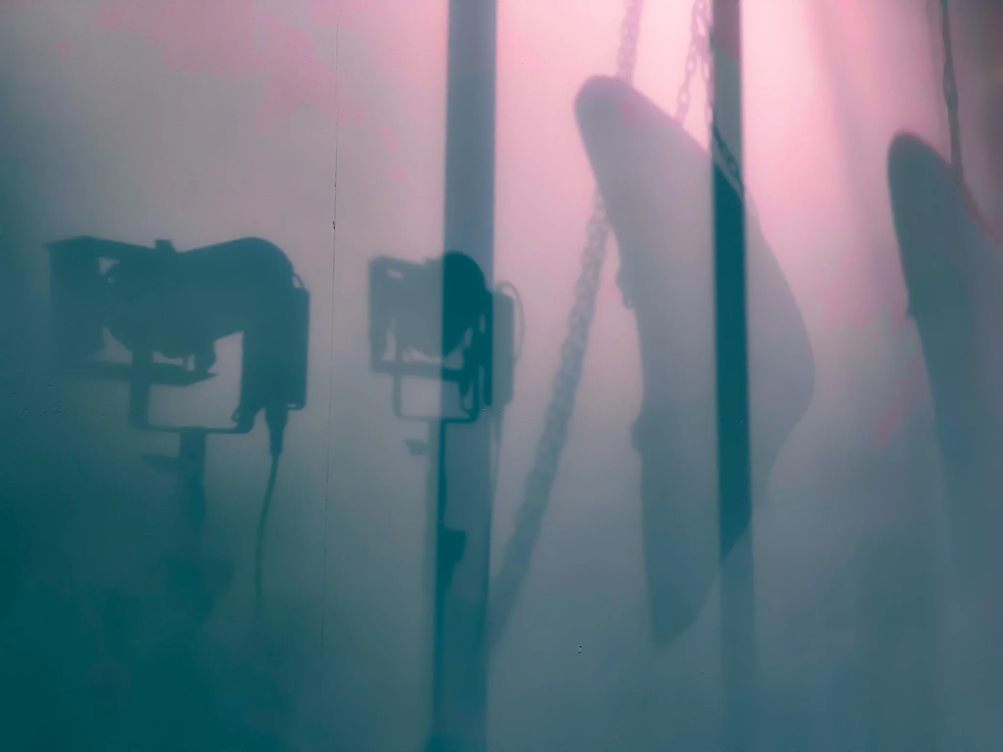 Shadows of hand-held art tools and a person's hand on a pink and blue gradient wall.