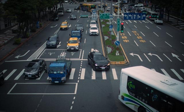 俯瞰城市大路口，汽車、公車與貨車行經畫滿標線的車道，台灣