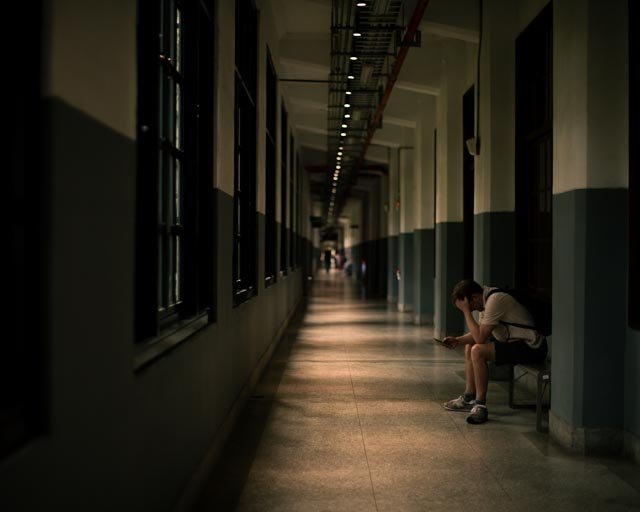 昏暗悠長的迴廊裡，年輕男子坐在長椅上低頭看手機，台灣