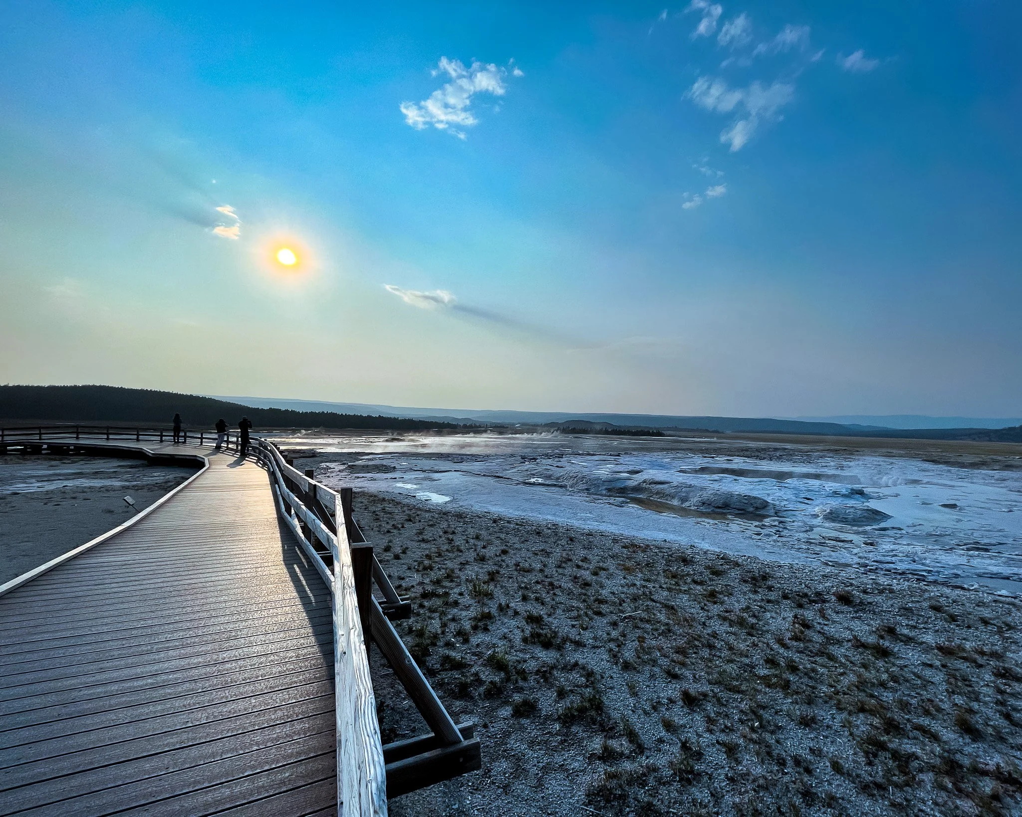 Boardwalk leading to a geyser basin with silhouetted figures, Yellowstone, 2021