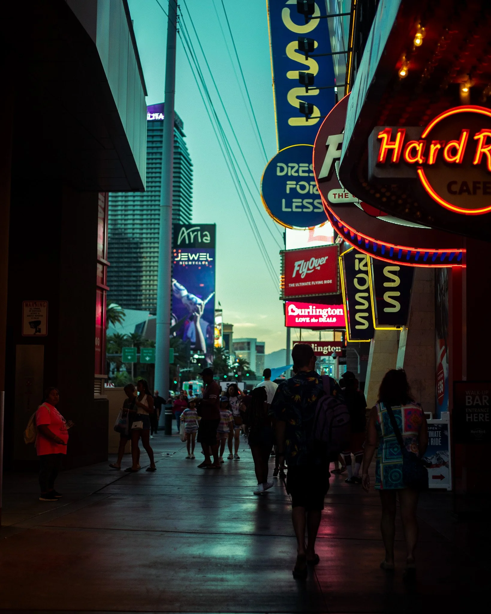 Silhouetted walkers beneath stacked neon signs at teal dusk, Las Vegas, 2023