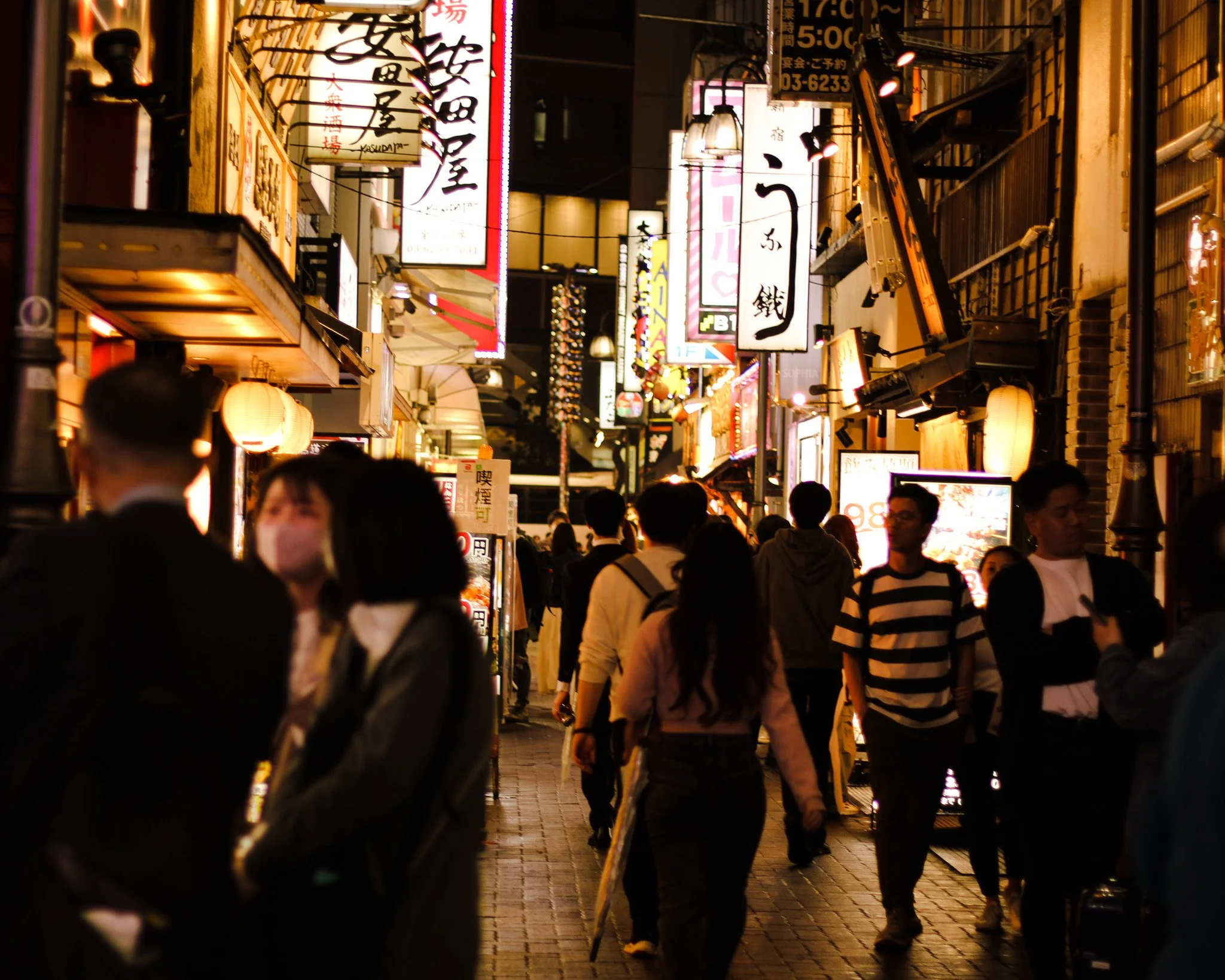 Night scene of a busy Japanese street with people walking under illuminated signs and paper lanterns.