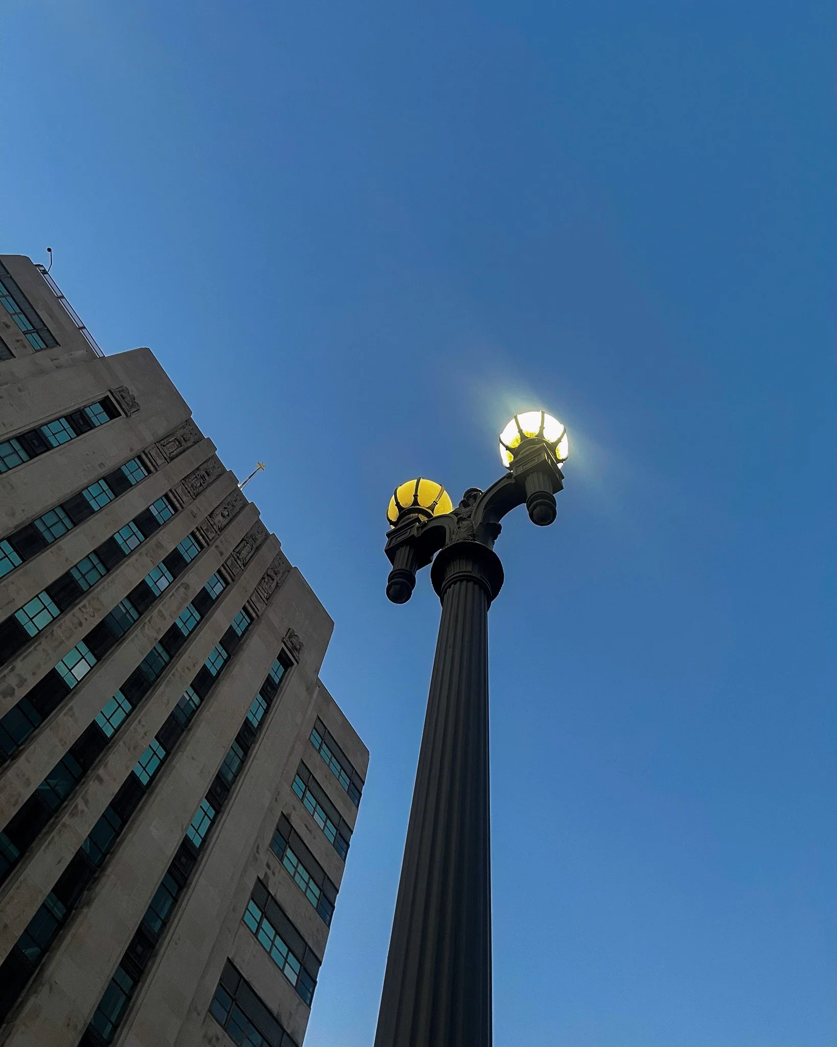 Ornate cast-iron street lamp against a clear blue sky beside an art deco high-rise, 2023