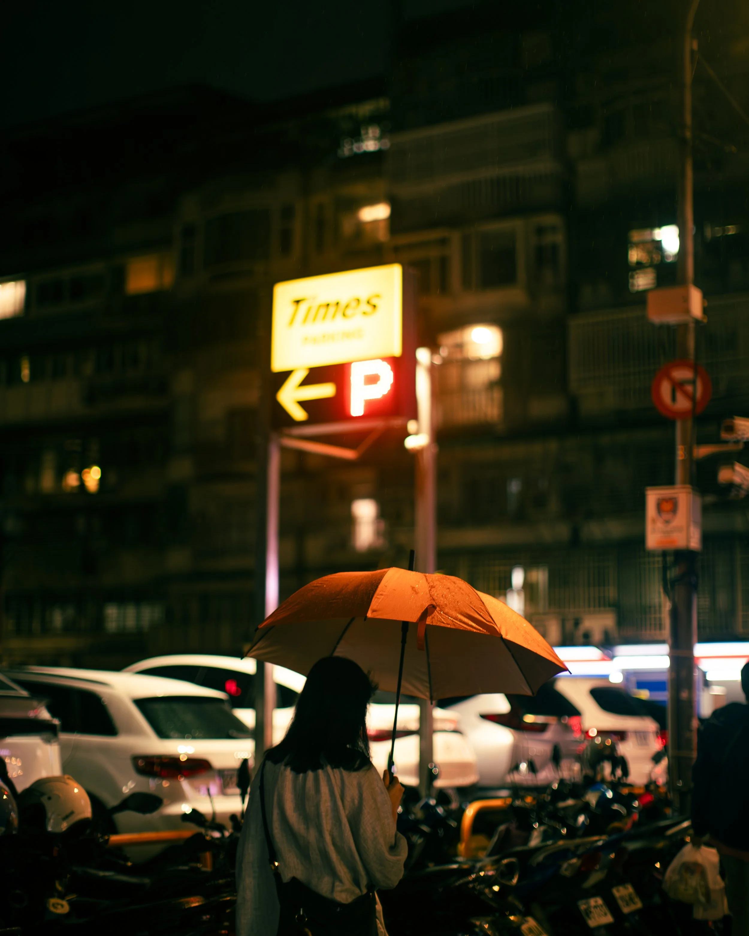 雨夜裡，女子撐著橘色雨傘站在發亮的停車場招牌下，台北