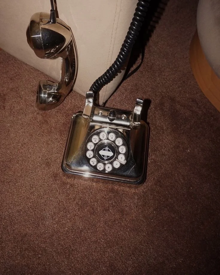 Vintage rotary phone in a metallic finish placed on a brown carpet next to a couch.