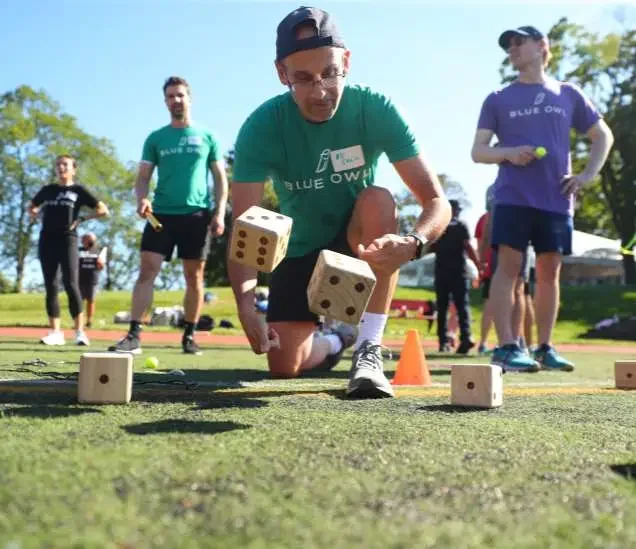People participating in an outdoor game involving large dice as part of a team relay on a grassy field.