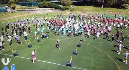 A large group of children and adults participating in an outdoor activity or game on a grassy field with various equipment and cones.