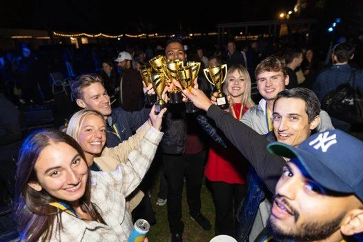 Group of people celebrating with golden trophies at night, smiling and raising their awards.