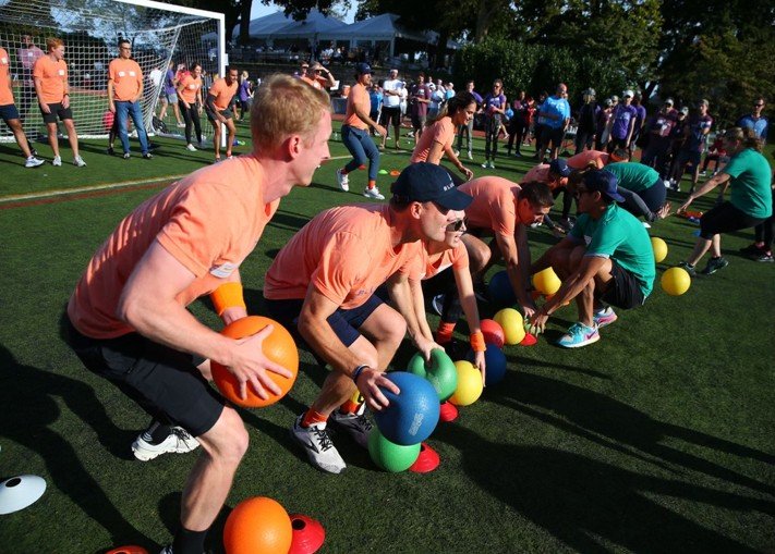 People participating in a group exercise or team-building activity using large colored balls on an outdoor sports field.
