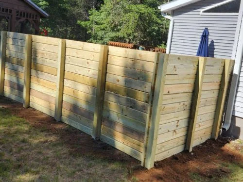 Newly built wooden privacy fence in a backyard near a house with gray siding and a blue umbrella.