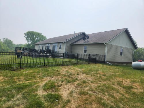 Residential house with a backyard enclosed by a black metal fence, with a propane tank in the yard.