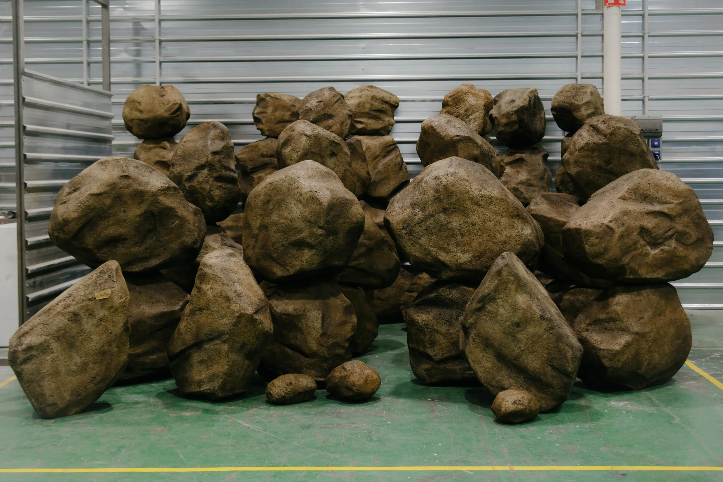 Grupo de rocas grandes apiladas en un espacio cerrado con paredes de metal y piso de color verde.