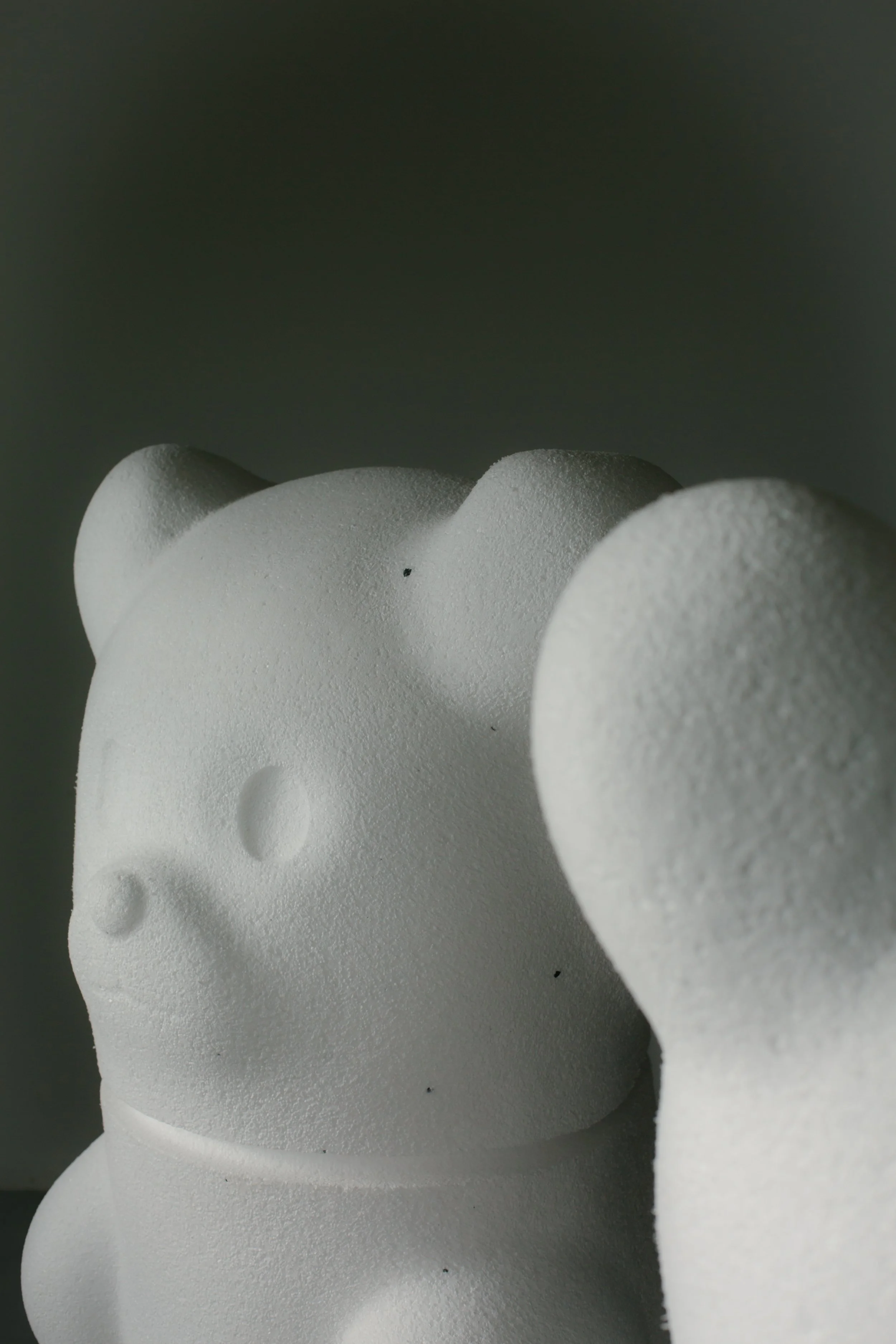 Figura de cerámica blanca con forma de esqueleto, vista lateral, con textura rugosa, contra fondo gris oscuro.