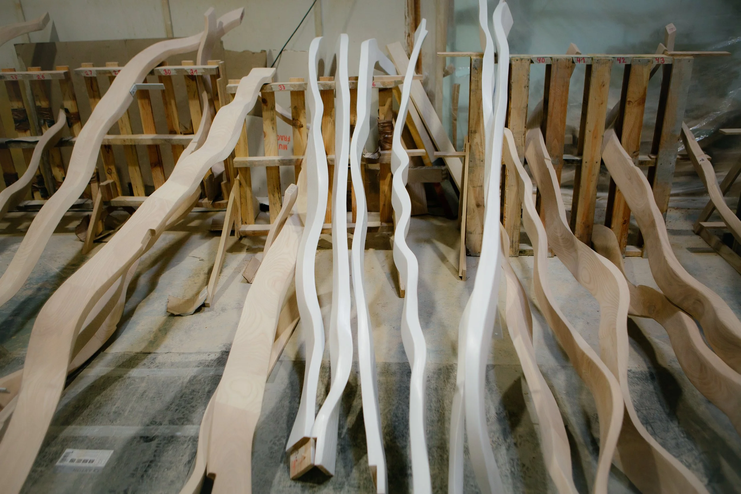 Taller de carpintería con varias piezas de madera curvadas y tablones de madera alineados en soportes.