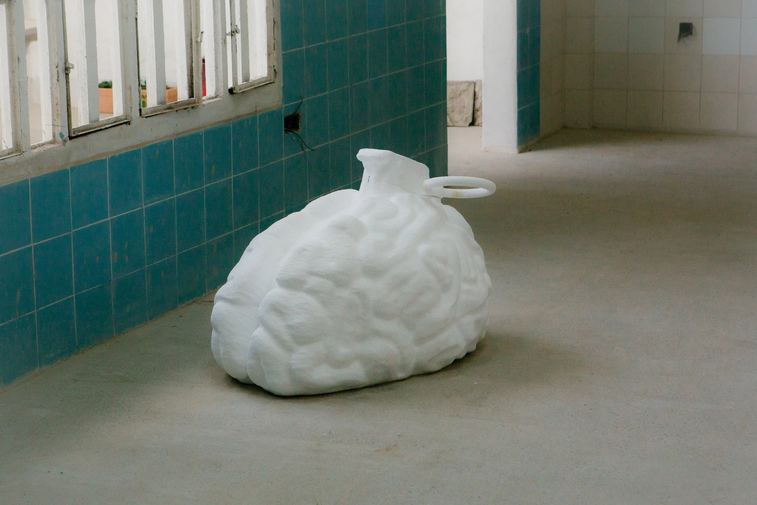 Sacos de plástico llenos con espuma blanca parecen ser utilizados para aislamiento o protección, colocados en el piso en un espacio interior con paredes y ventanas con barrotes.