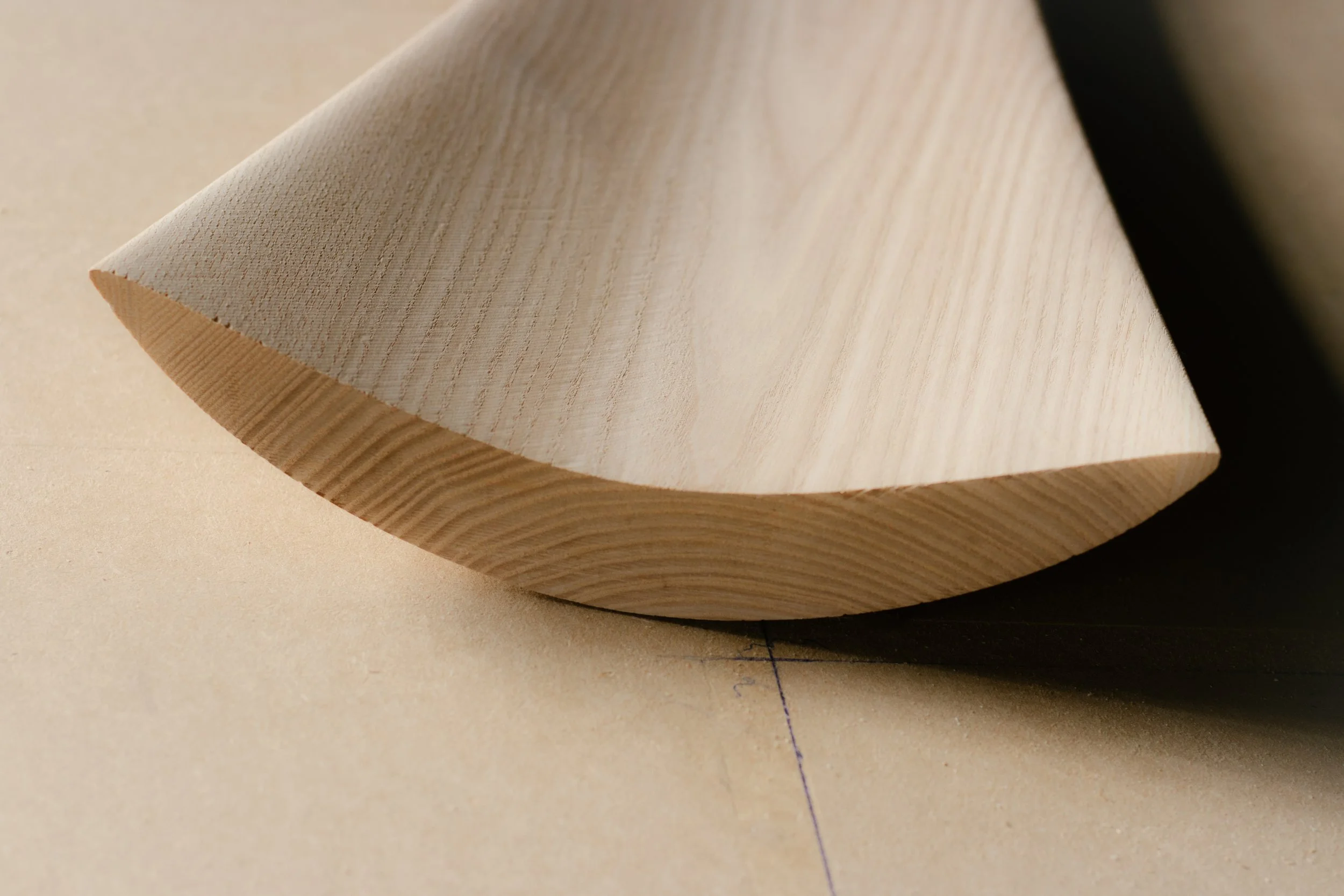 Trozo de madera de forma cónica, con textura visible y color claro, apoyado sobre una superficie de color beige.