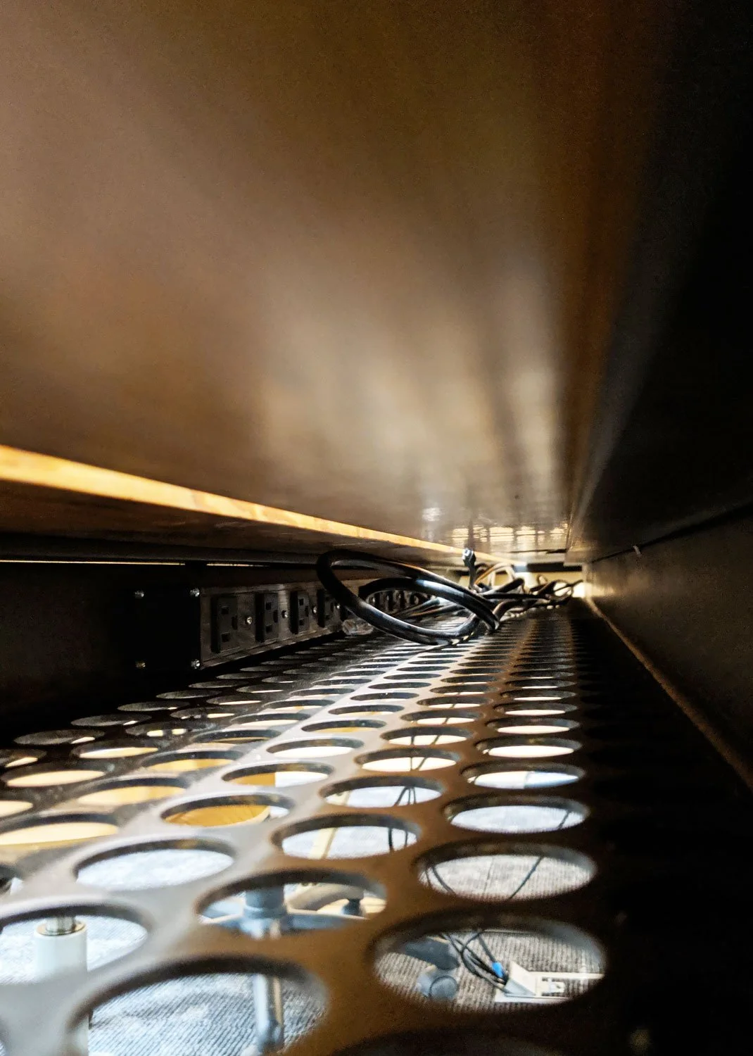 The underside of a table with a perforated metal cable tray with an integrated plugmold.