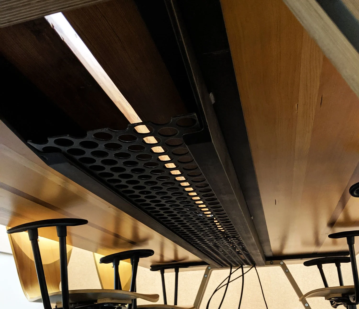 View of the underside of a wooden table with a perforated steel data cable tray.