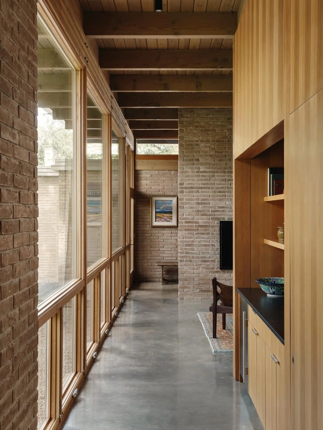 Hallway with large windows on the left, brick walls, wooden beams on the ceiling, and built-in wet bar on the right.