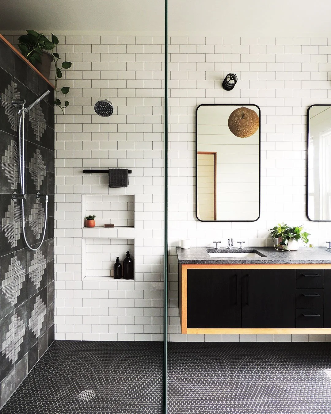 Modern bathroom with a walk-in shower featuring dark patterned tiles, white subway tiles, a built-in nook, and a floating vanity with a gray countertop with two rectangular mirrors above.