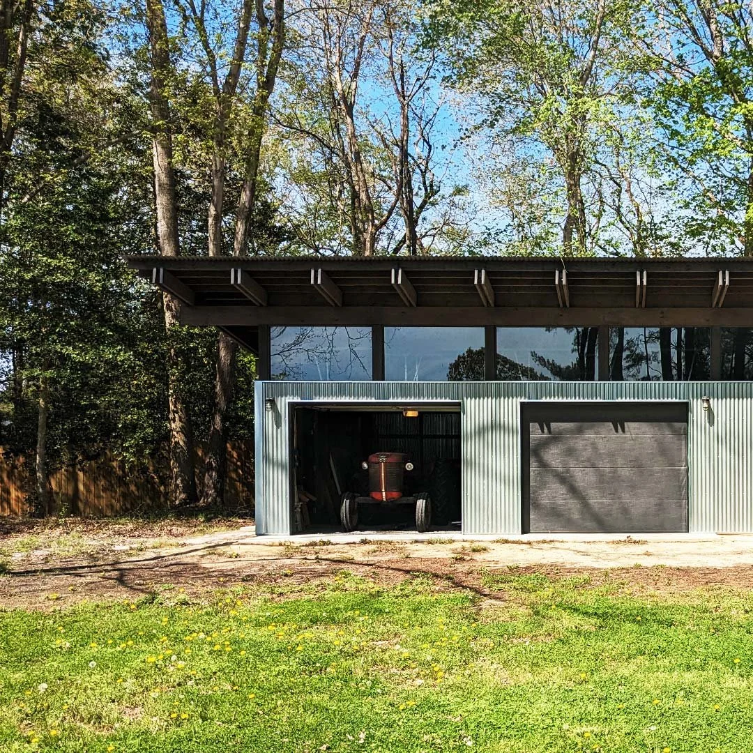A metal shed with an open garage door revealing an old tractor inside.