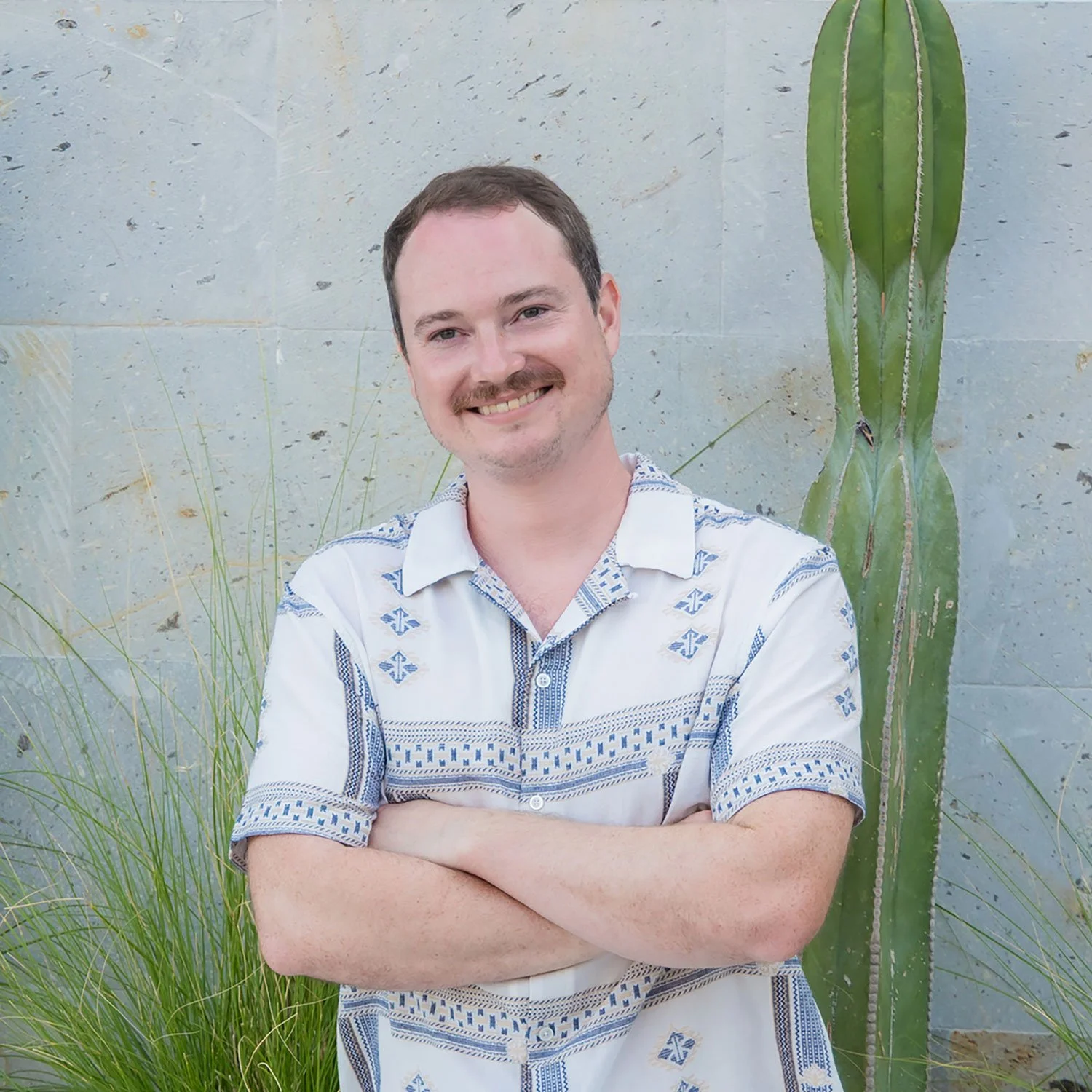Headshot of Robert Lingo with crossed arms in front of a cactus, tall grasses, and a stone wall.