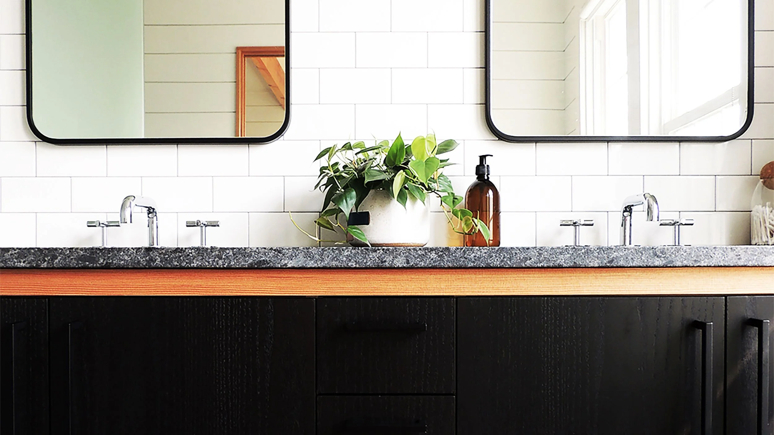 Bathroom vanity with dark cabinet doors, a granite countertop, two shiny chrome faucets, and two rectangular mirrors on a white tiled wall.