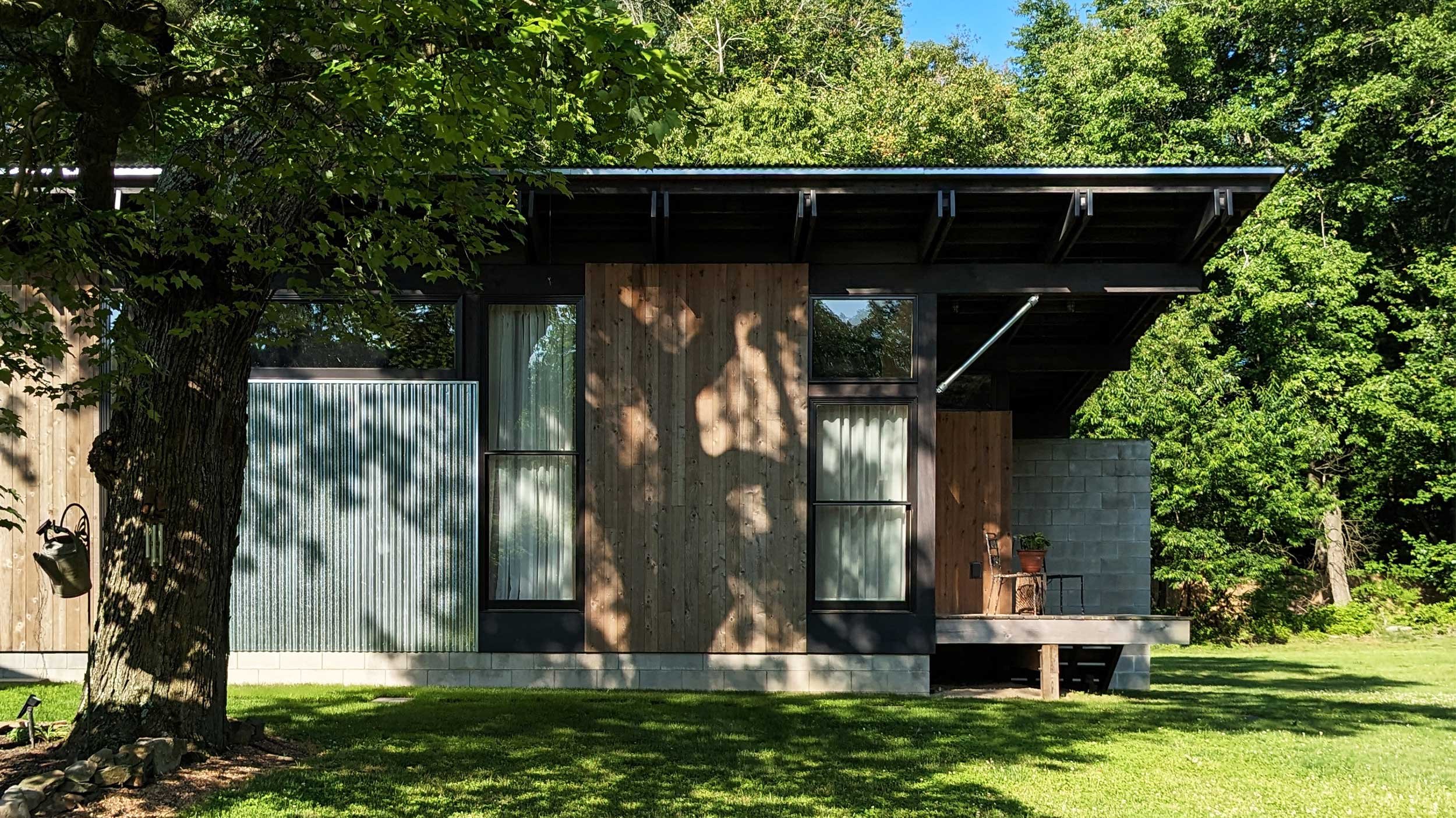 A modern house with a combination of wood, metal, and concrete exterior, surrounded by green trees and grass.