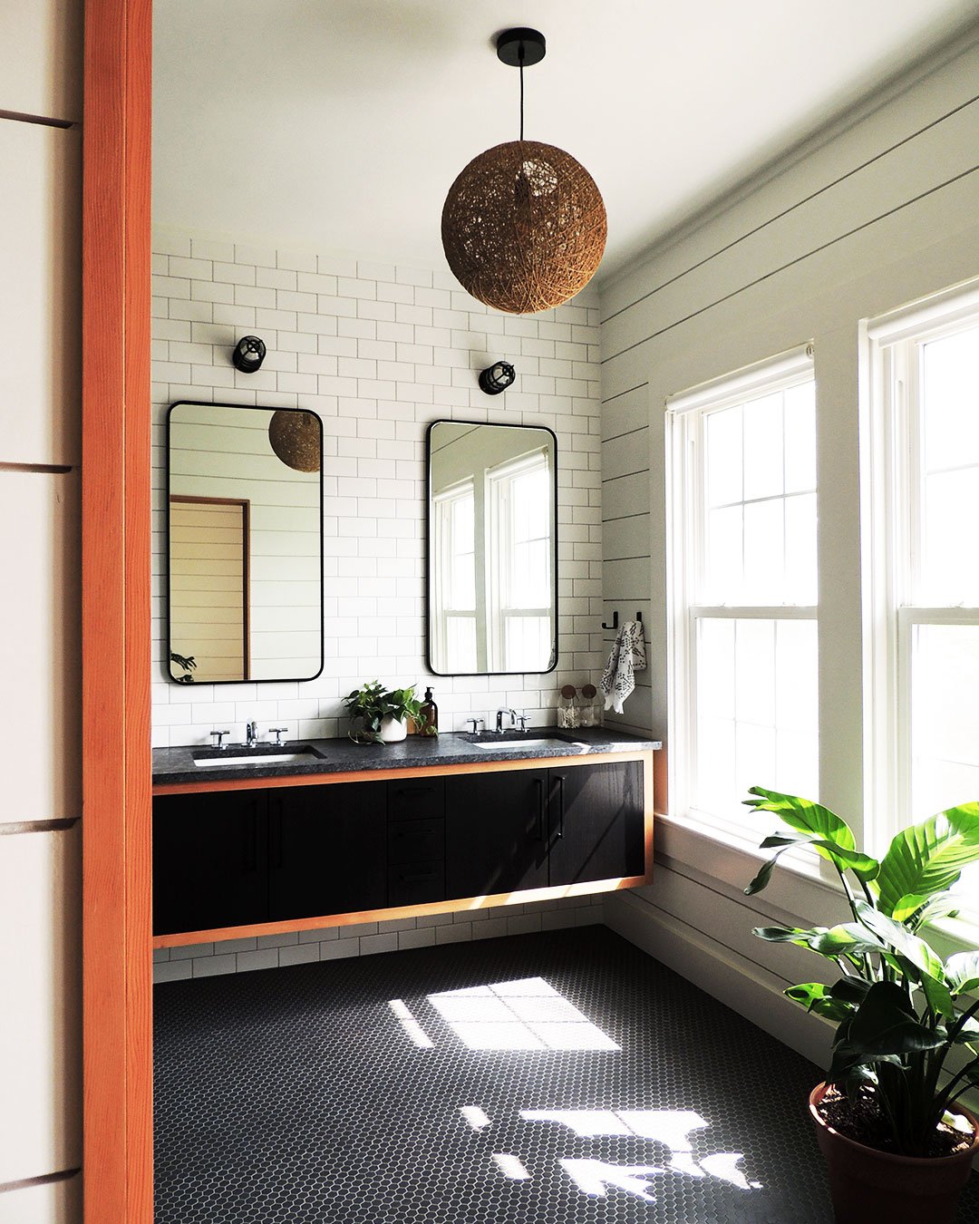 Modern bathroom with floating vanity, white tiled wall with two mirrors, and natural light from large windows.