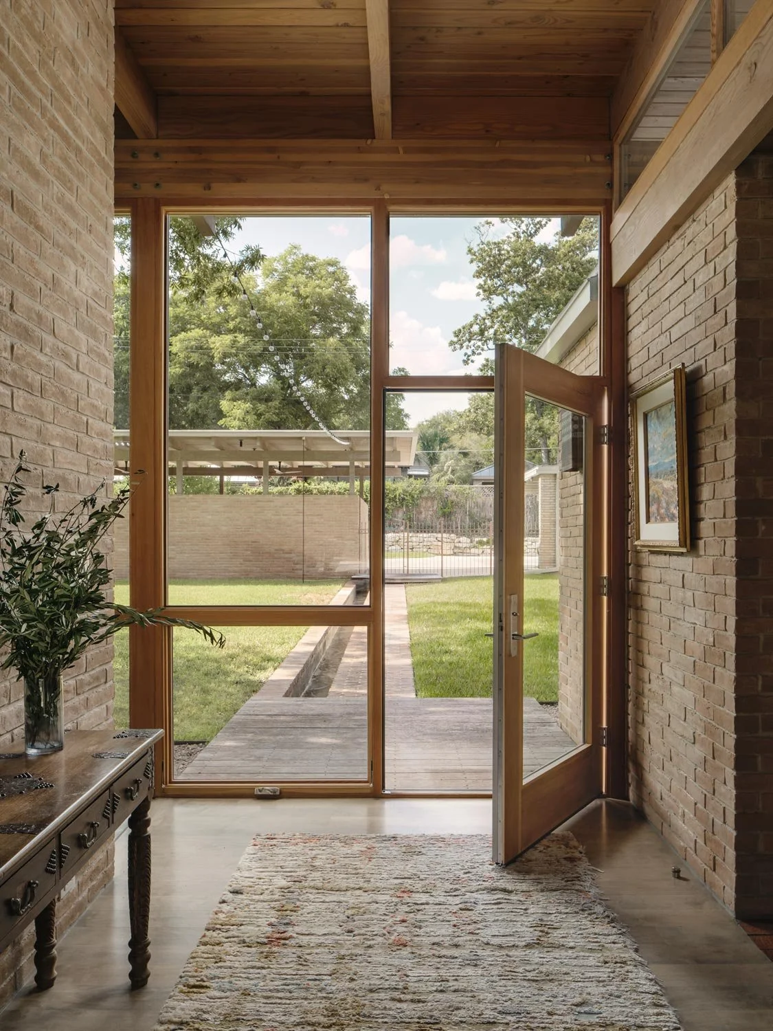 Interior view of an entryway with a large glass door and windows, brick walls, looking out toward a grassy courtyard.