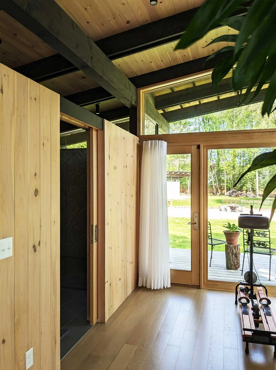 Interior of a modern home with wood walls and large glass door leading to a backyard with outdoor furniture and greenery.