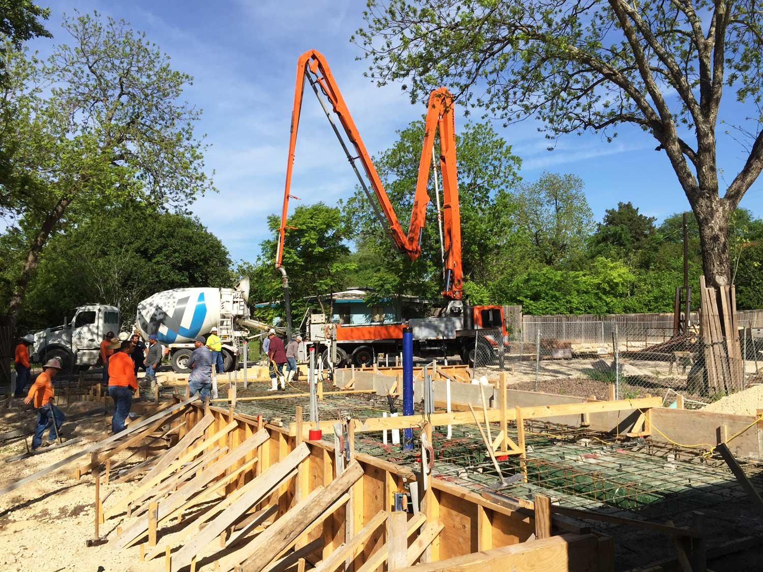 Construction site with workers pouring concrete using a large orange concrete pump.