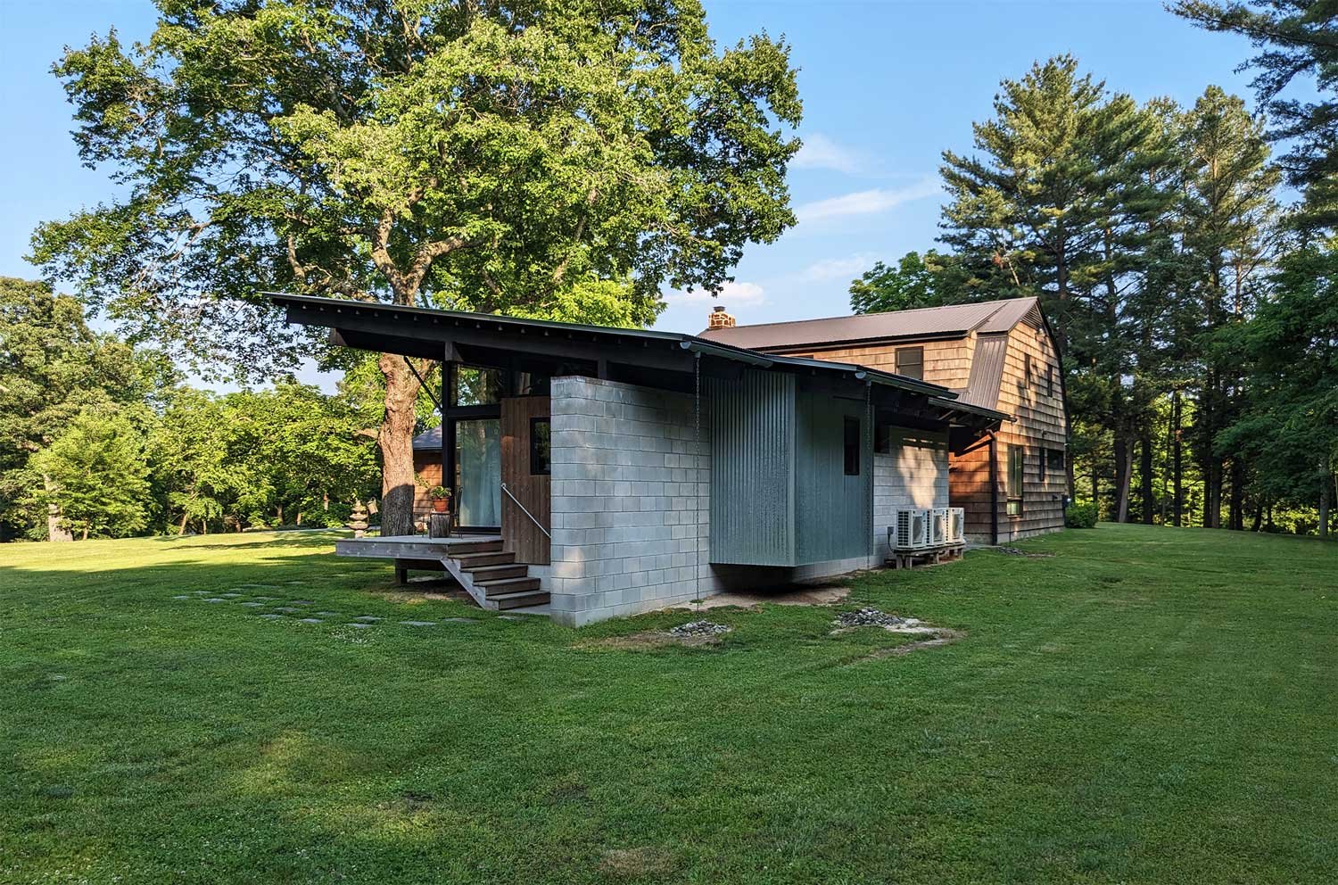 Modern house with a mix of wooden and concrete exterior, surrounded by green lawn and trees, under a clear blue sky.