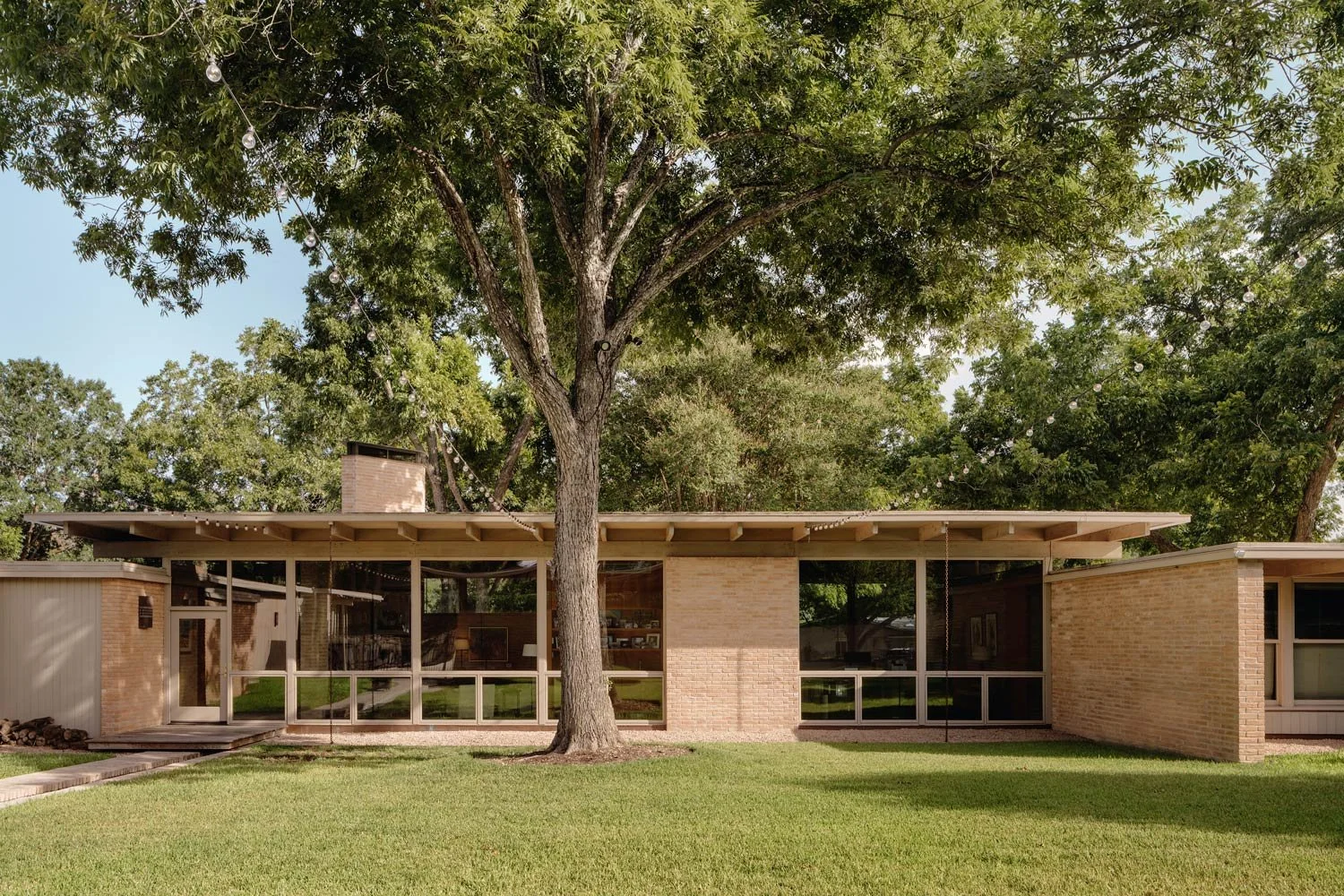 Mid-century modern house with large glass windows, brick walls, and a flat roof.