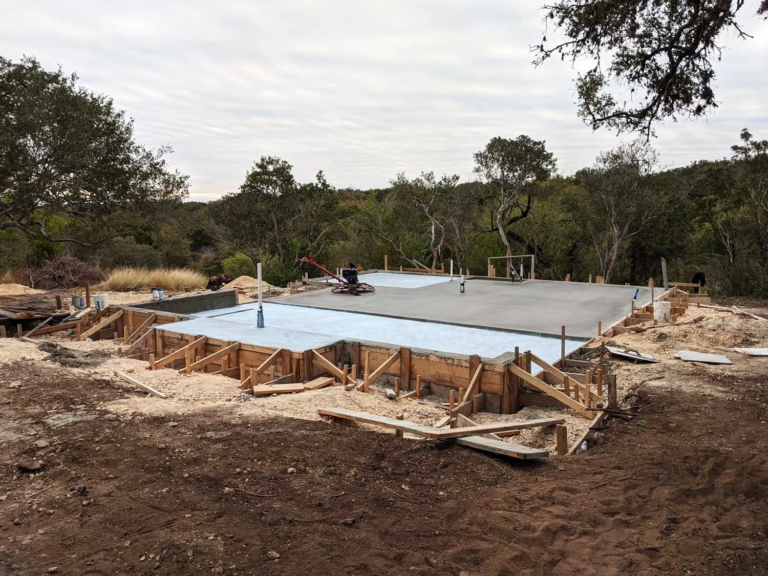 Construction site with a concrete foundation in progress in a wooded setting.
