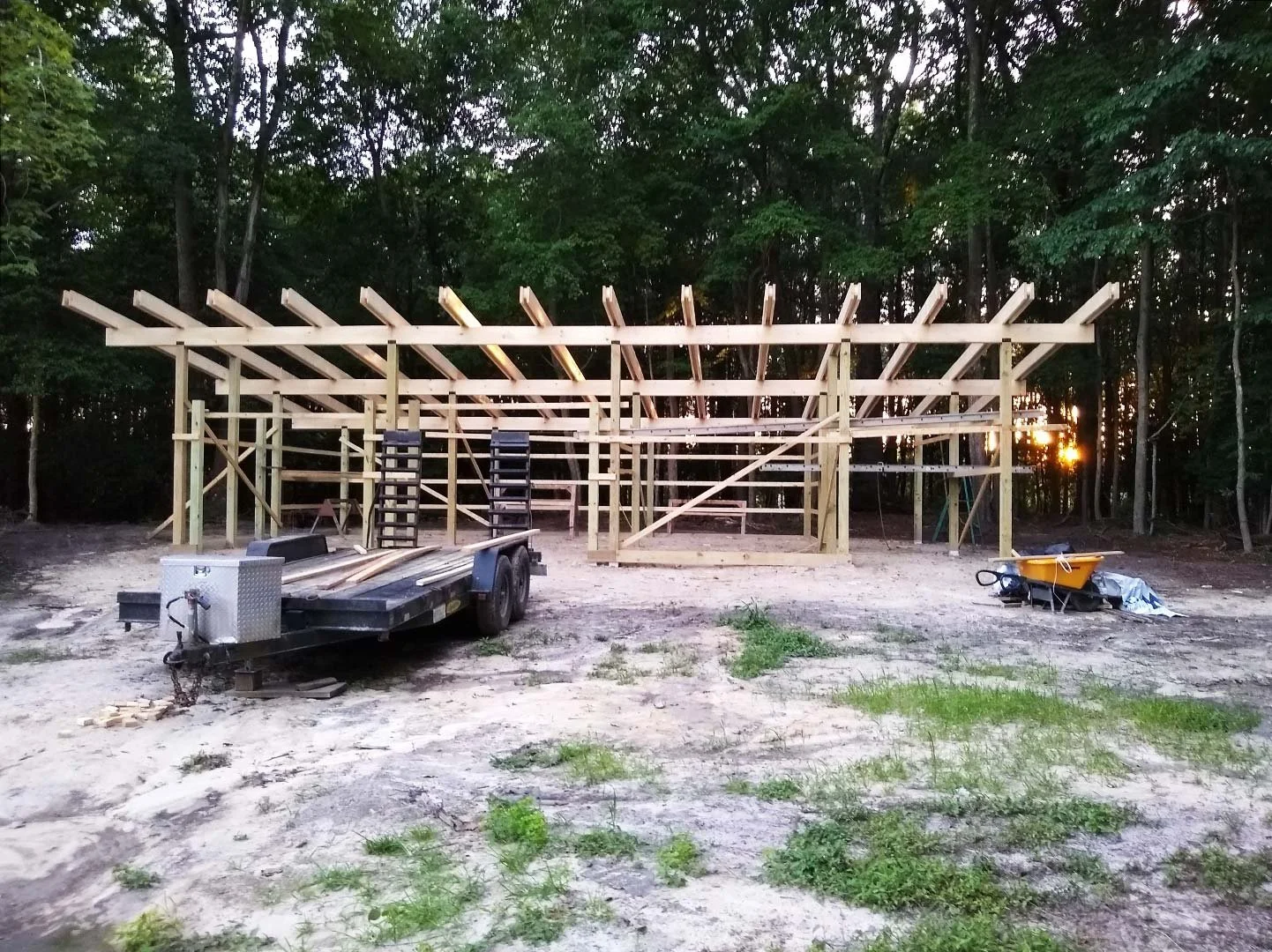 Wooden frame structure under construction on dirt ground with trees in the background.