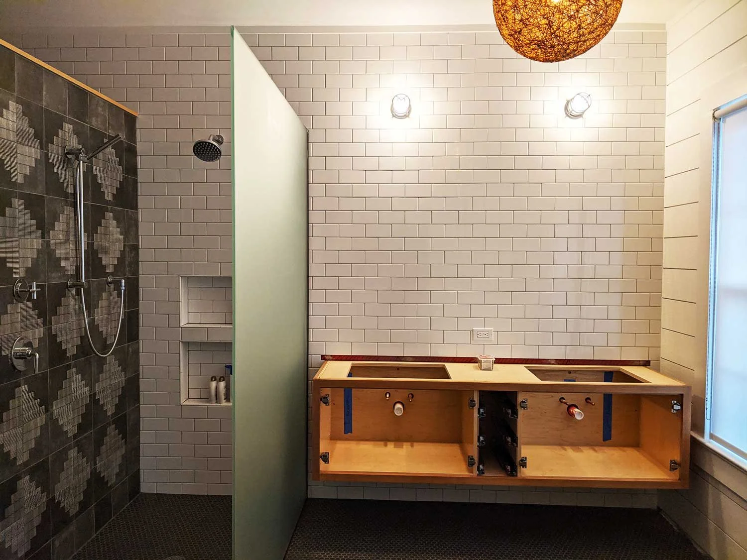 Bathroom under construction with shower area, tiled walls, partially installed wooden vanity, and frosted glass partition.