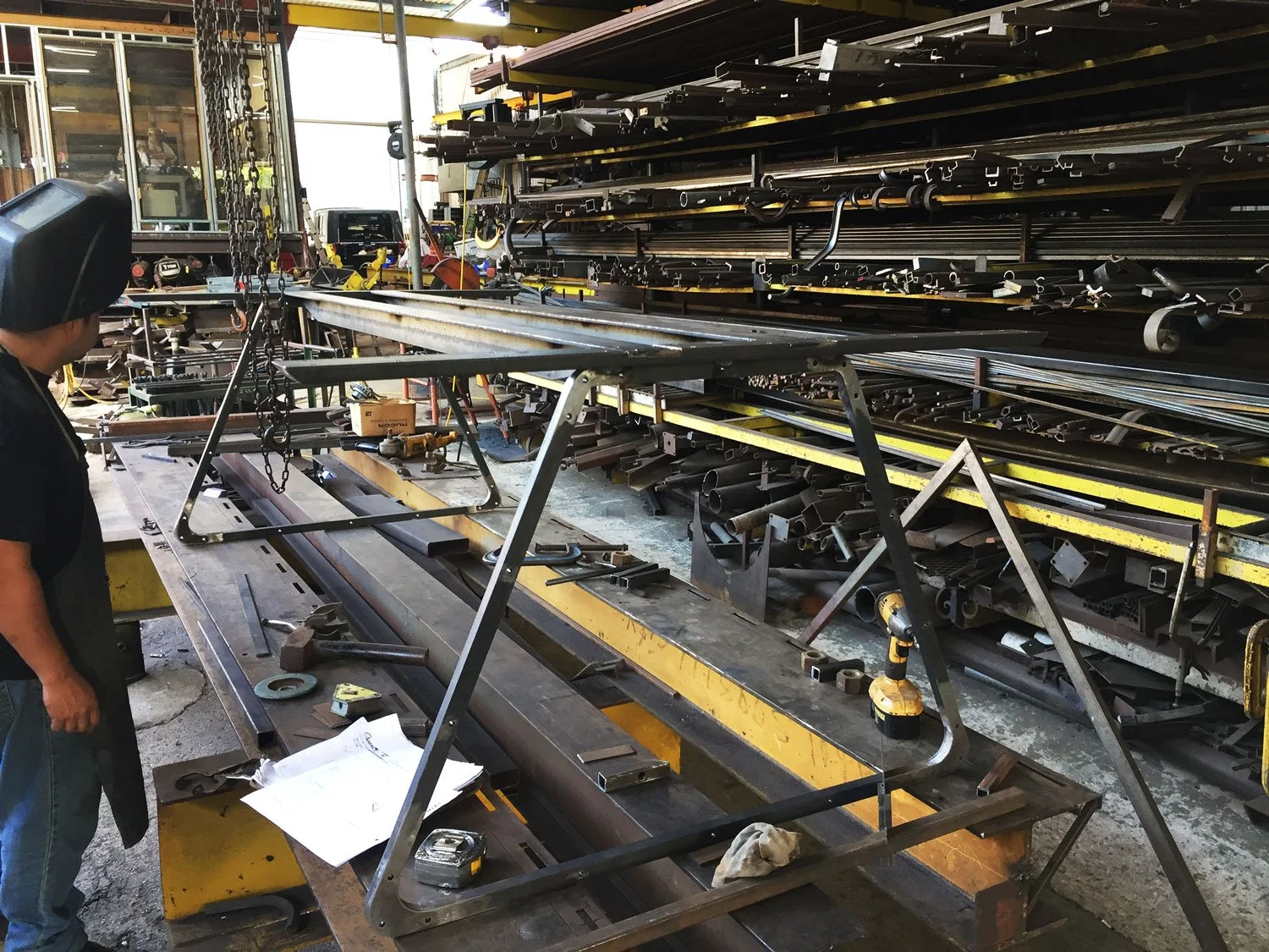 Metal table frame being worked on in an industrial workshop, surrounded by metal pipes, tools, and equipment.