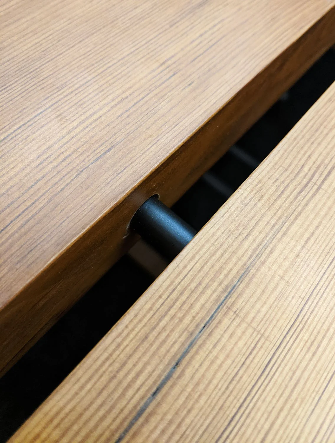 Close-up of a wooden table's center gap with a black metal support dowel.