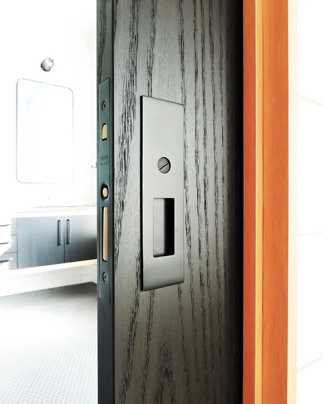 Close-up of modern pocket door hardware on a dark wooden door.