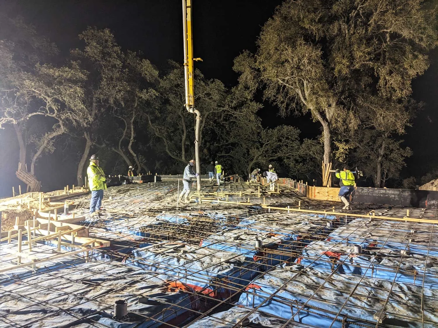 Construction workers pouring concrete on a building foundation at night.