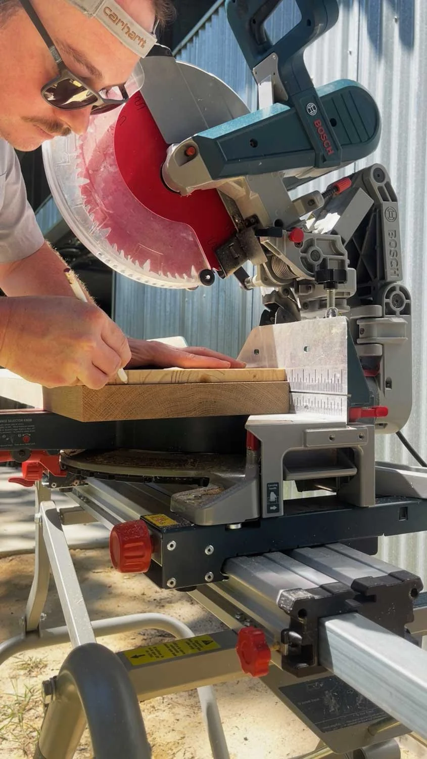 Man operating a miter saw to cut a wooden board outdoors.