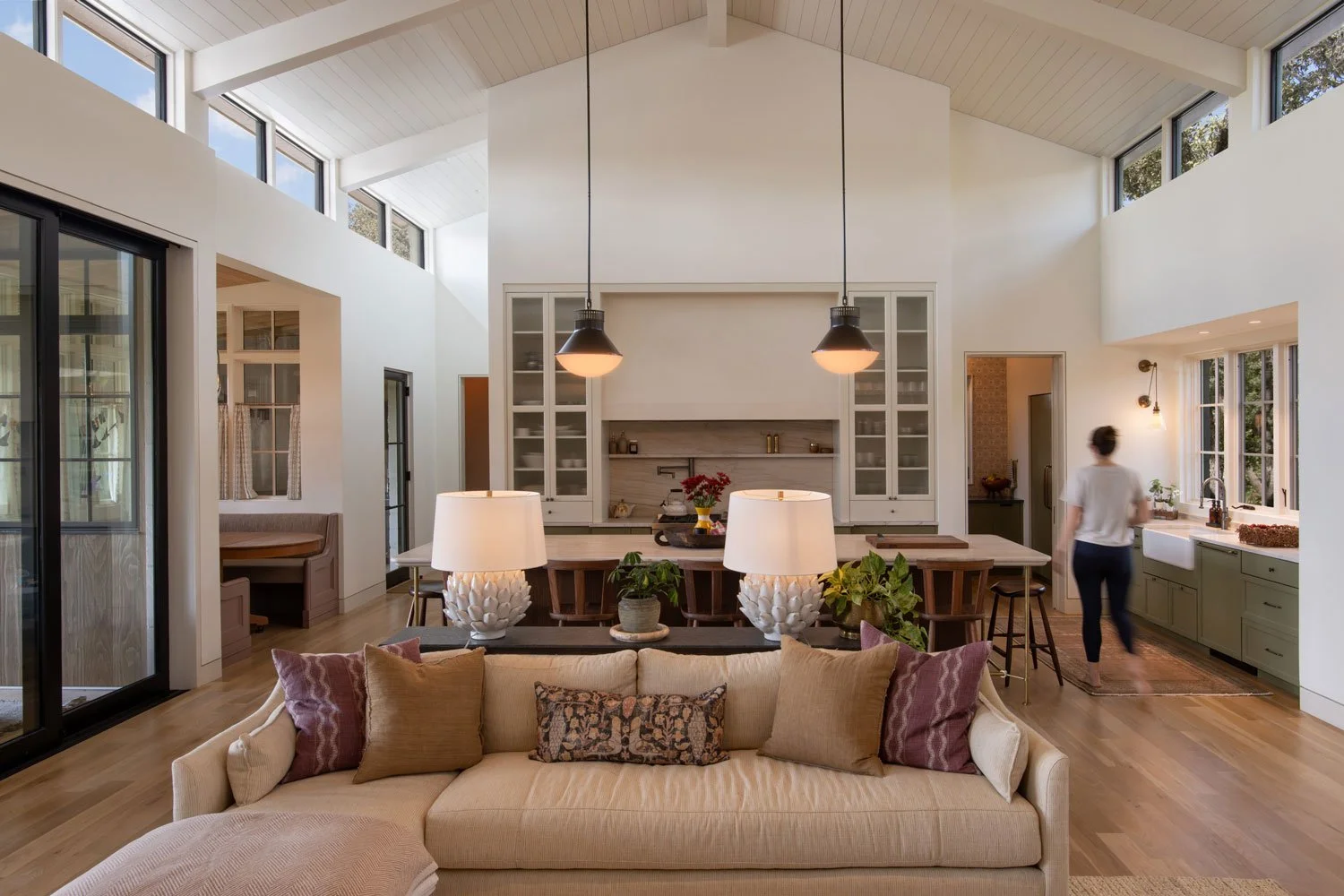 Open-concept living room and kitchen with high vaulted ceiling, large windows, and wood floors.