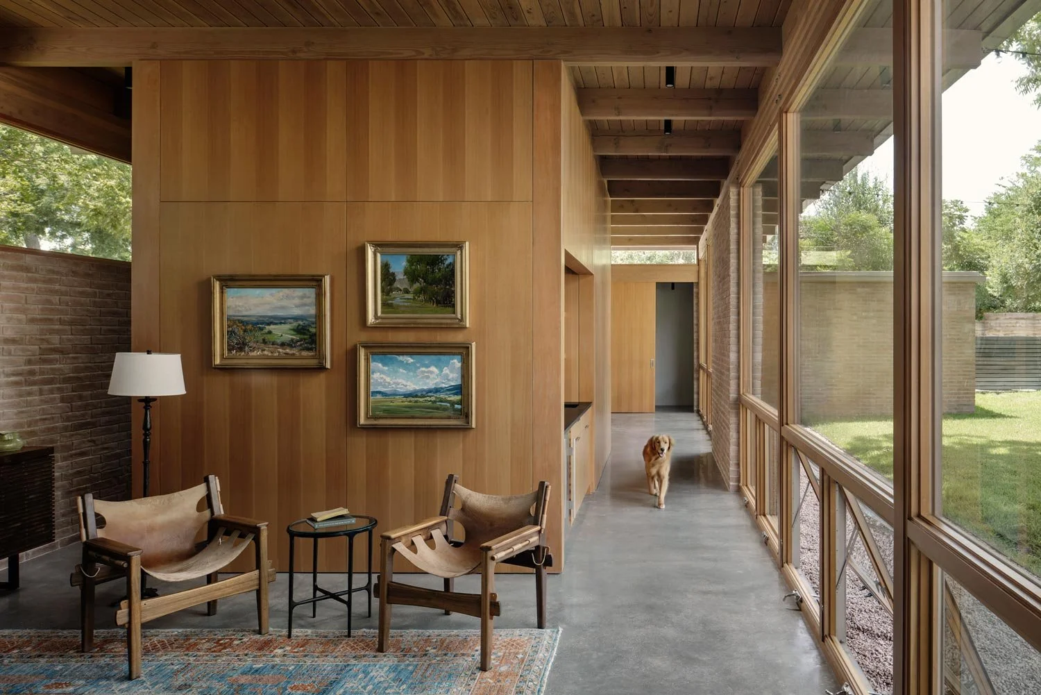 Interior view of a modern home with wooden and brick walls, large windows on the right, and a seating area.