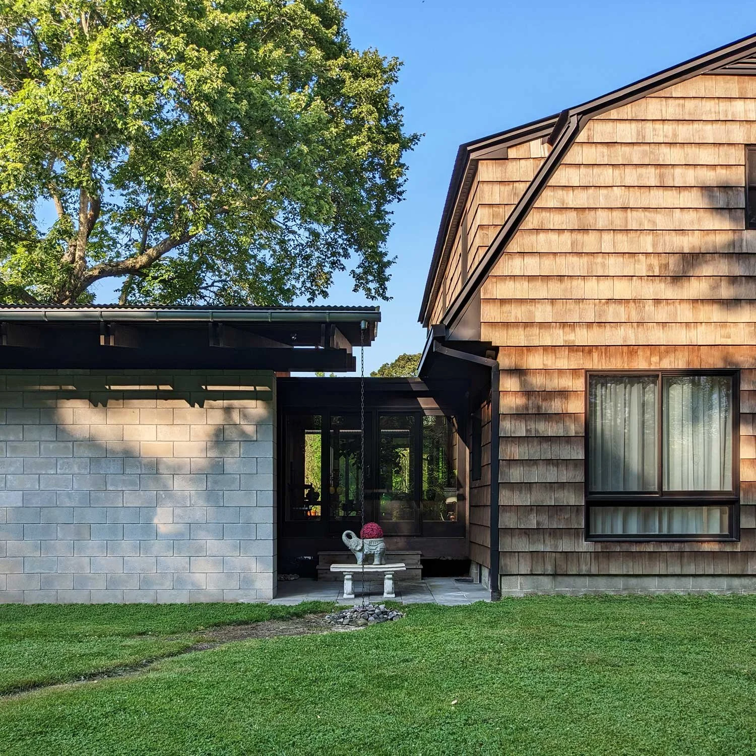 A modern home addition with CMU wall connected to a house with cedar shake siding, joined by a glazed connecting breezeway.