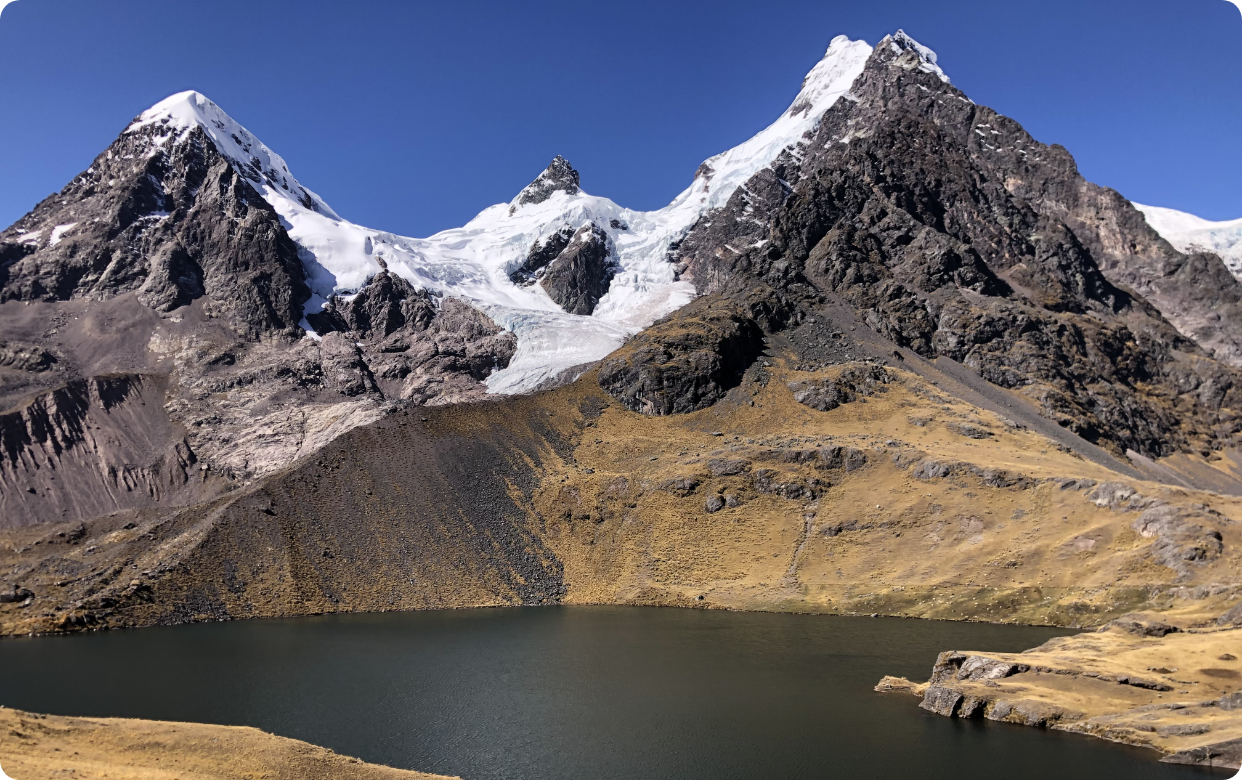 Snow-capped mountains with a glacier, a mountain lake, and dry grassy slopes in the foreground.