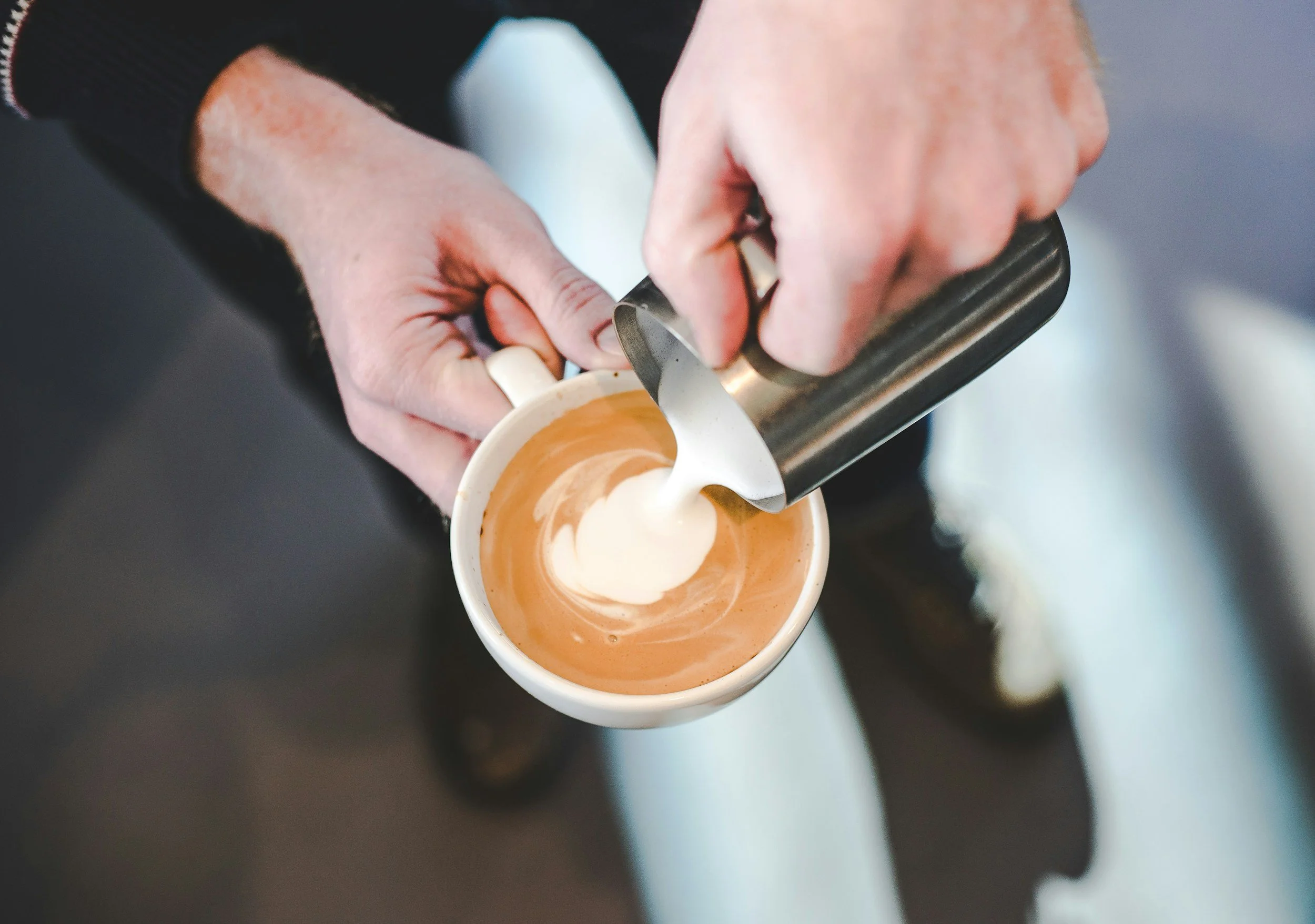 A person pouring steamed milk into a cup of espresso to make a latte.