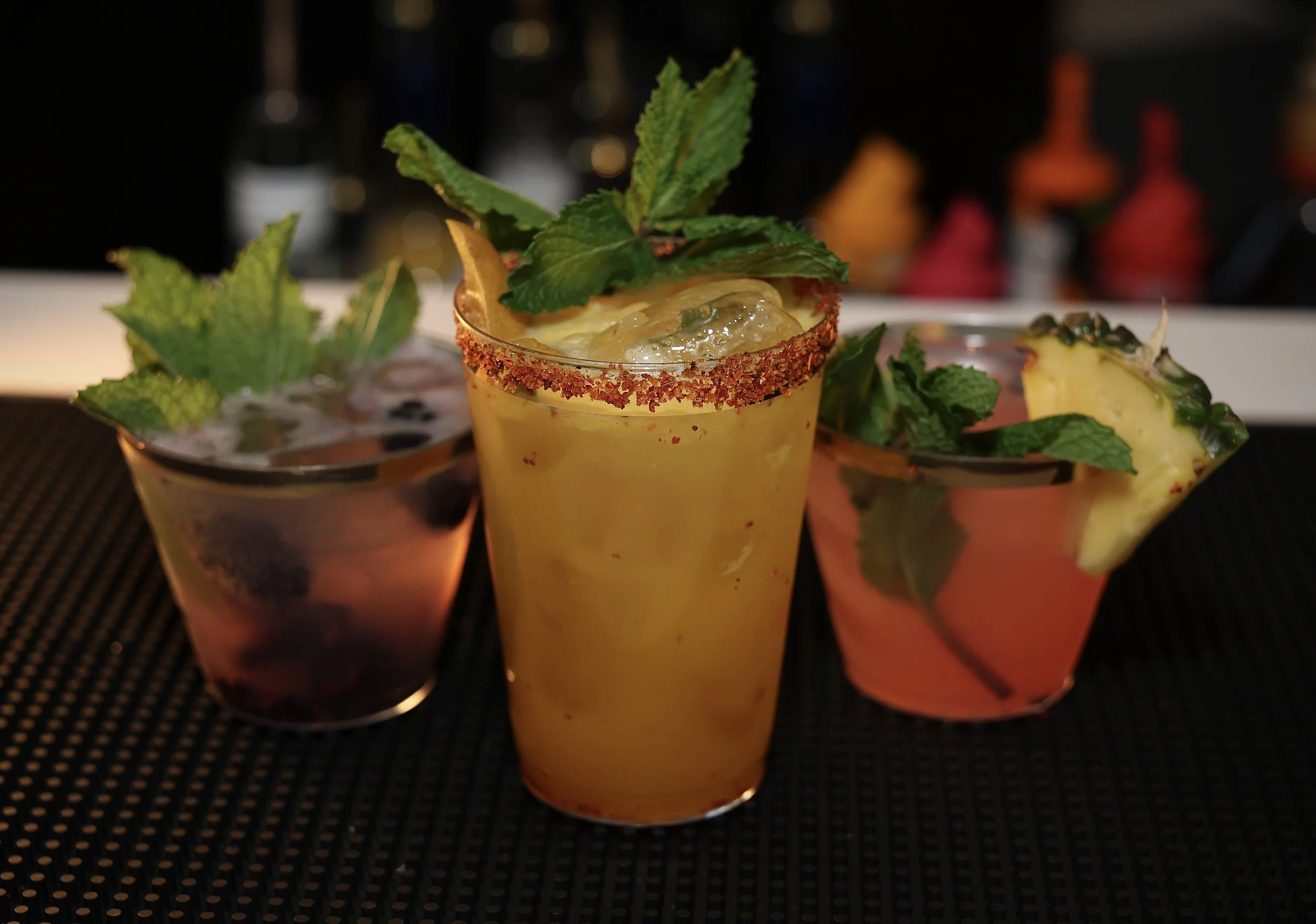 Three cocktails garnished with fruit and mint leaves on a black surface.