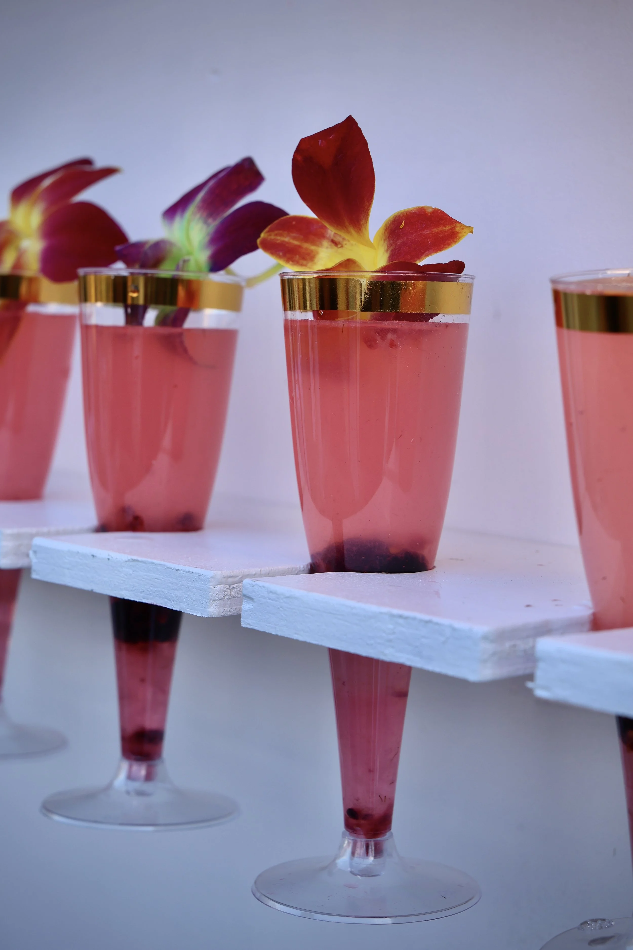 Several pink cocktails with orchid garnishes arranged on a white display shelf.