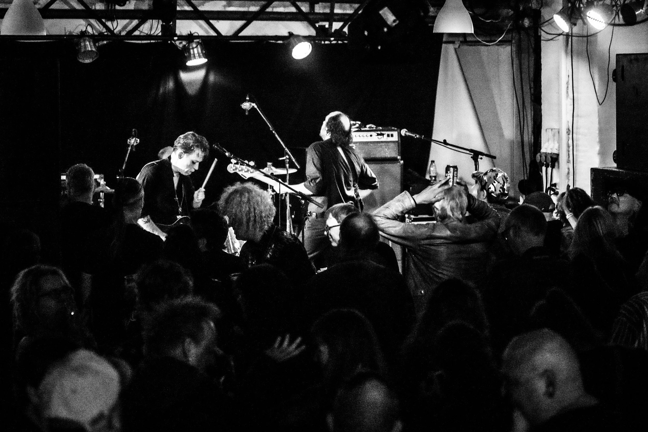 A black and white photo of a live music performance in a small venue with an audience.